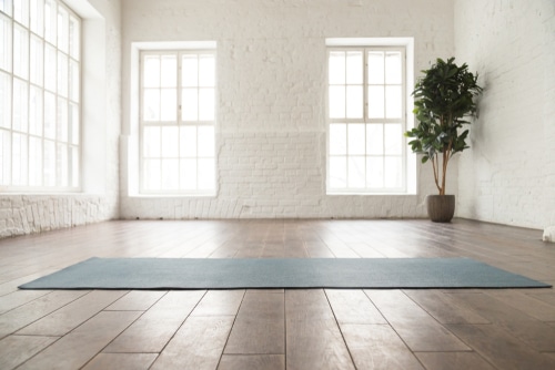 A well lit and airy meditation room with a single gray mat.