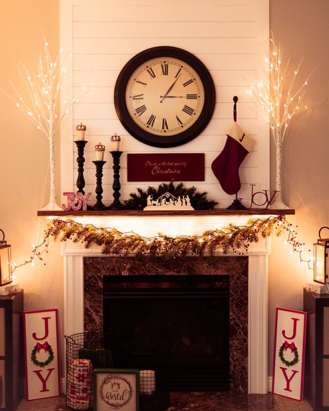 A simple wooden fireplace with Christmas lights and decorations.