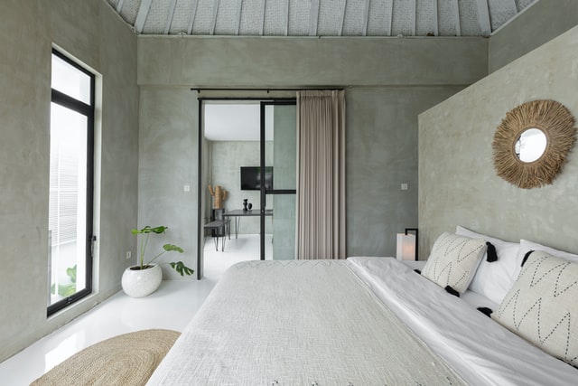 concrete finish bedroom A simple bedroom with white sheets, round decorative mirror, and concrete finish walls