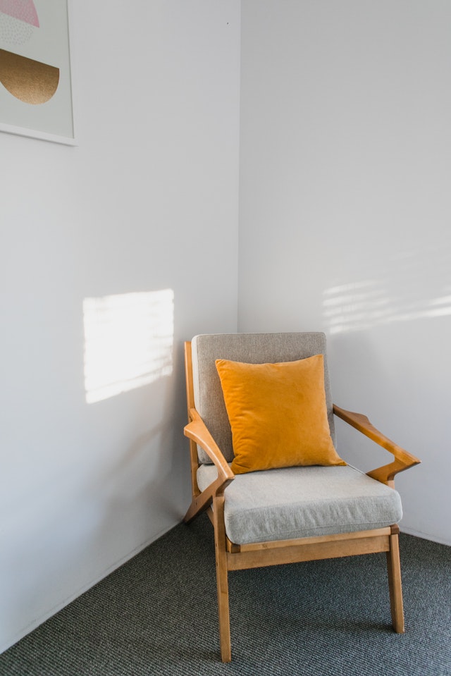 A simple chair with bright orange pillow looked like a decor against a plain white wall.