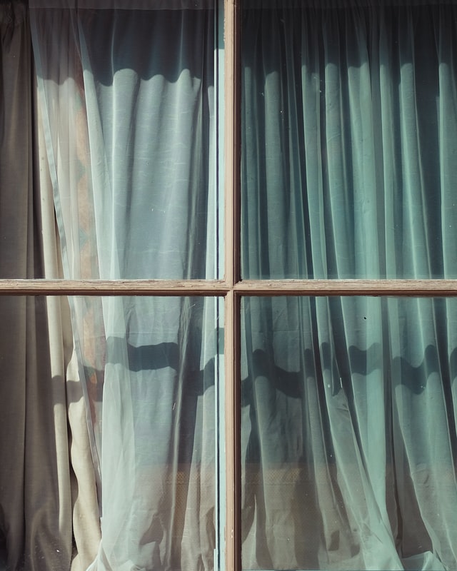 A closeup picture of a glass window with inside curtains.