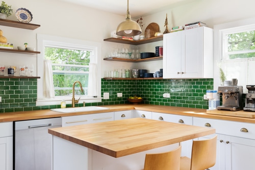 A very homey kitchen using a wooden countertop and green subway tiles backsplash.