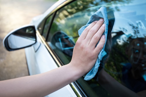 A hand wiping outside windows of a white car