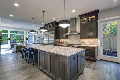 A modern kitchen with a long granite kitchen island and darkwood cabinetries.