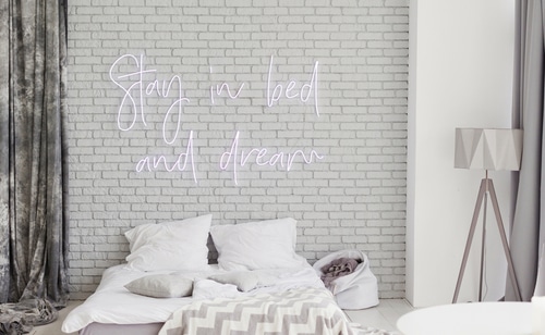 Minimalist modern bedroom with neon sign on a white brick wall.