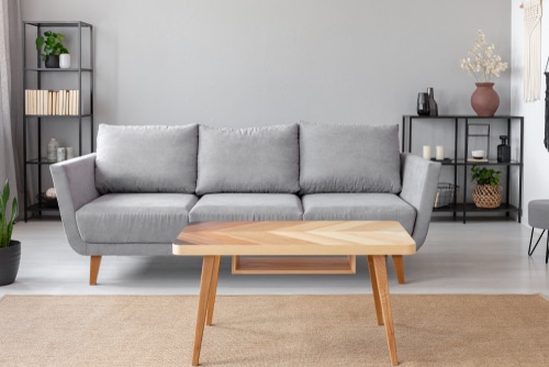 A small wooden table with a pattern coupled with a modern gray couch.