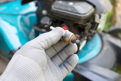 A person holding a spark plug from the lawn mower