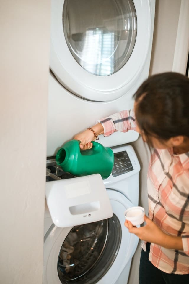 A woman pouring a liquid detergent into the washing machine dispenser.