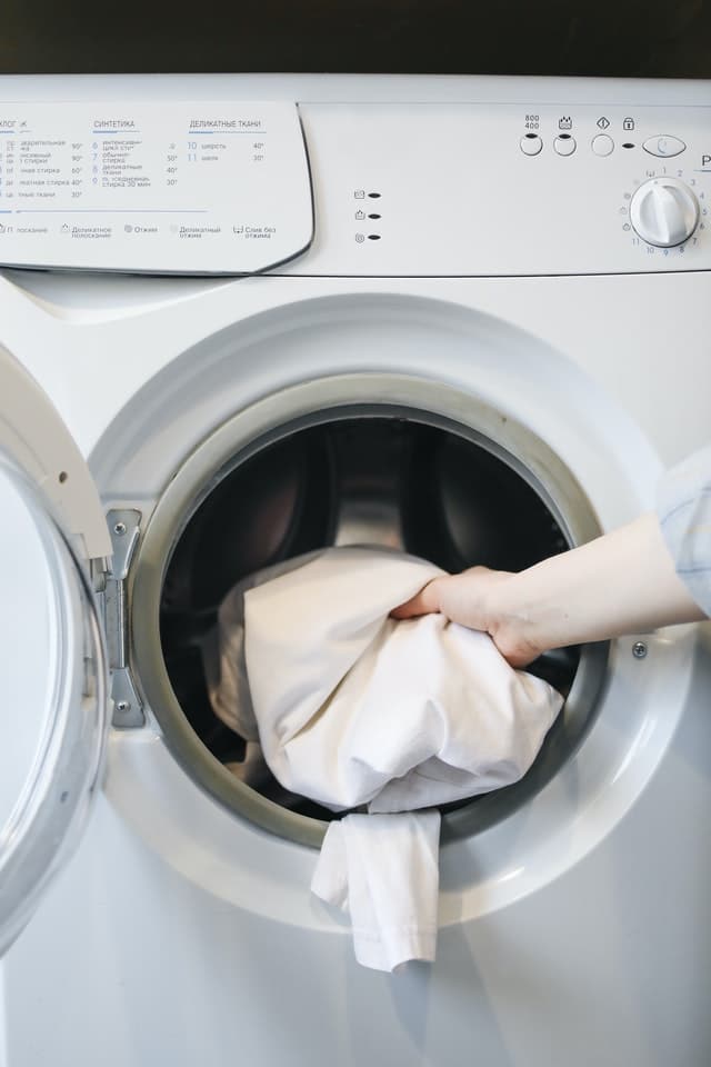 A person putting a white cloth in a washing machine.