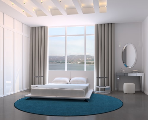 A well lit simple white bedroom with a round blue rug.