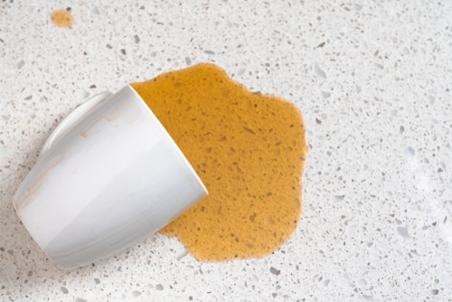 Spilled orange juice over a white quartz from a white mug.