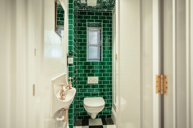 A narrow toilet space with an accent wall using green subway tiles.