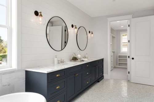 Two round mirrors whit black frames for his and hers sink in a white bathroom.