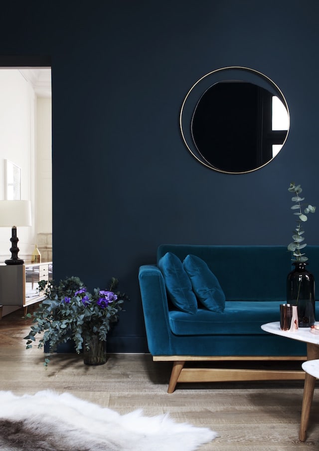 A velvet texture pop blue green sofa against a dark blue wall