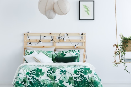 A white room with plant print beddings and wooden bed frame with string lights.