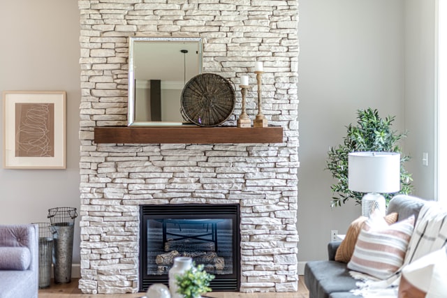 A modern fireplace using white bricks with a hanging wooden shelf with decors.