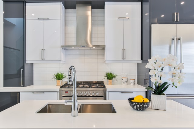 A gray and white kitchen with white counter and stainless sink