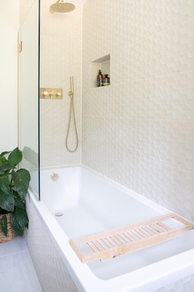 A rectangular shaped corner tub with a glass enclosure and gold fixtures.