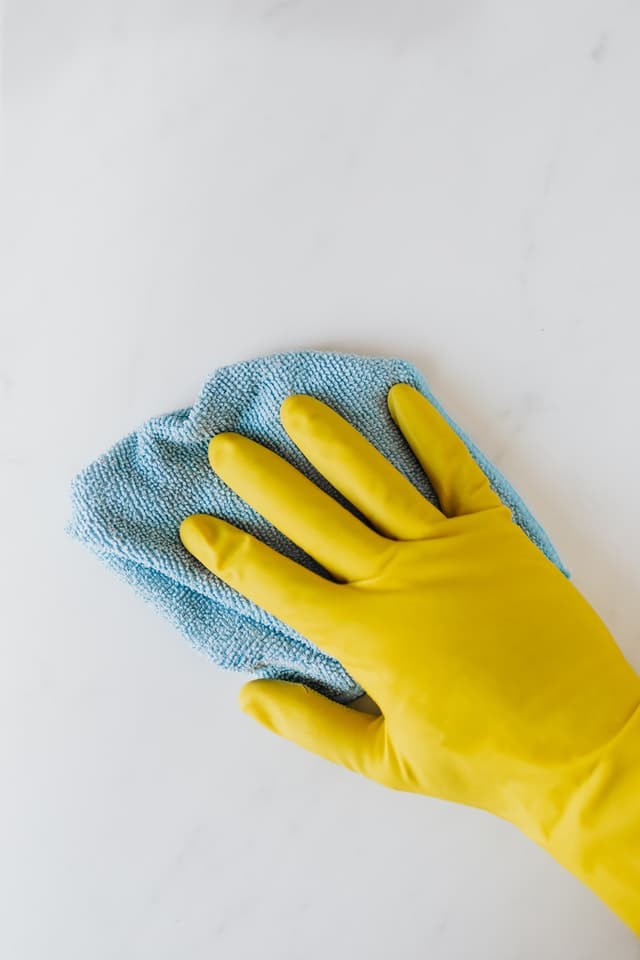 A hand with yellow gloves wiping a surface using a cloth.